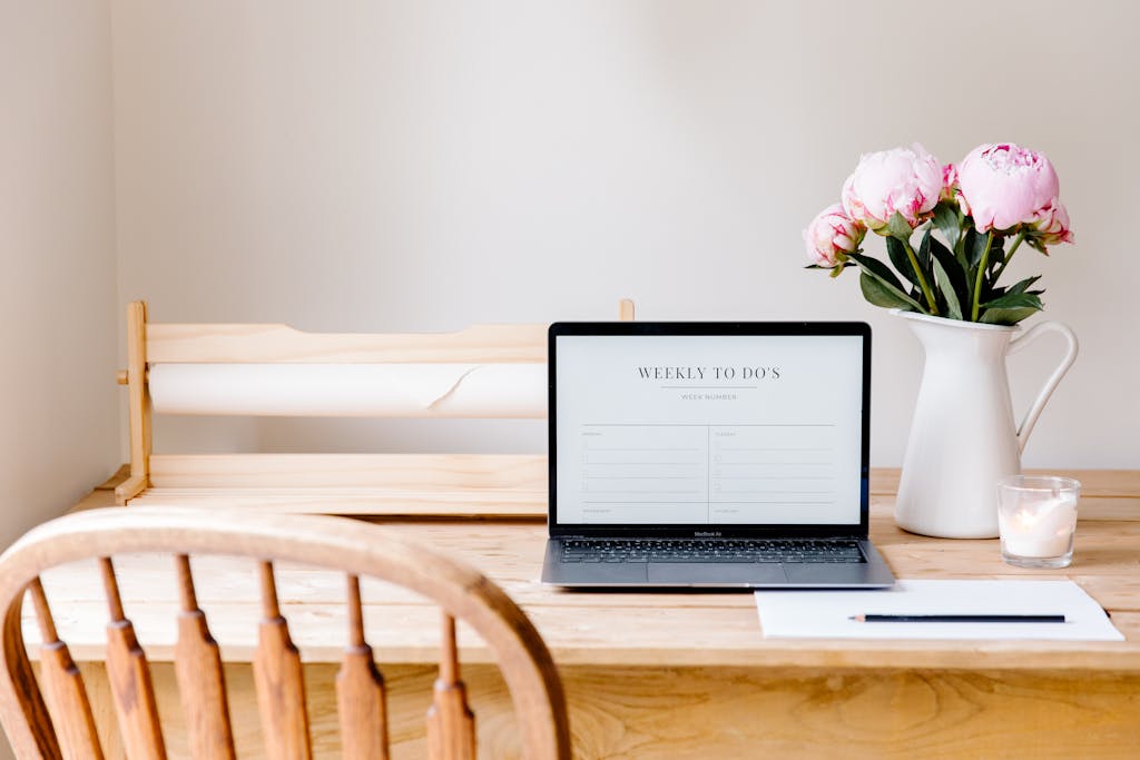A stylish home office setup featuring a laptop, flowers, and writing materials.