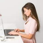 A woman in a pink dress working on a laptop at a modern, minimalist desk.